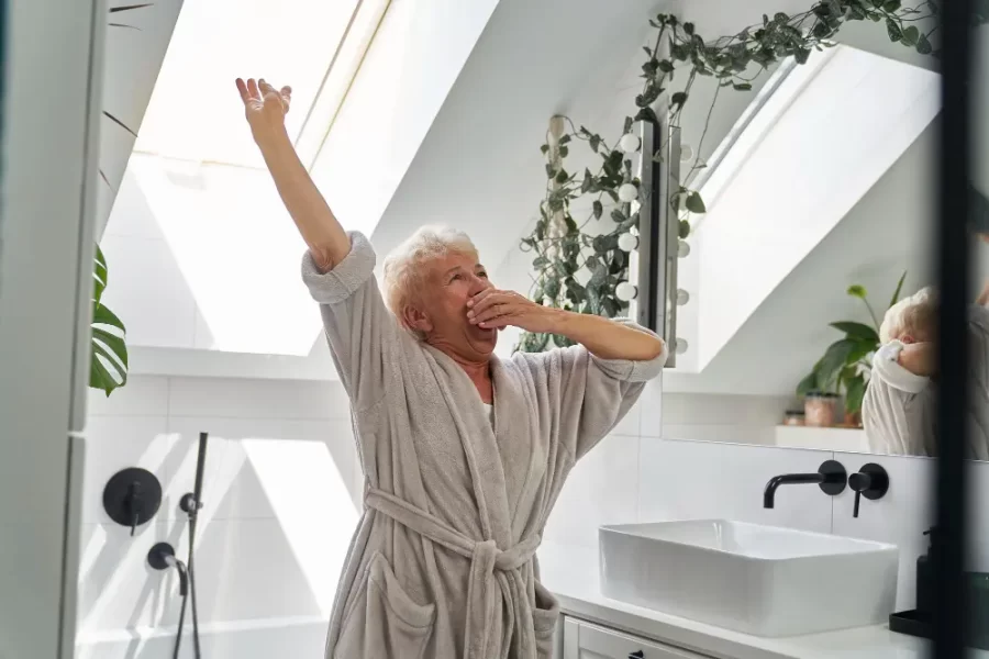 Elderly woman stretching in a bright bathroom.